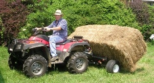 Person on ATV using a Big Bale Mover to move a large bale of straw