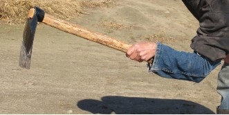 An arm holding a hoe with a denim cuff over the forearm, wrist, and end of the hoe's handle.