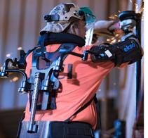 A person using an angle grinder on a piece of metal while wearing an exoskeleton.