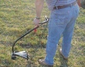 An image of a person from the waist down using a string hammer in a patch of green grass.