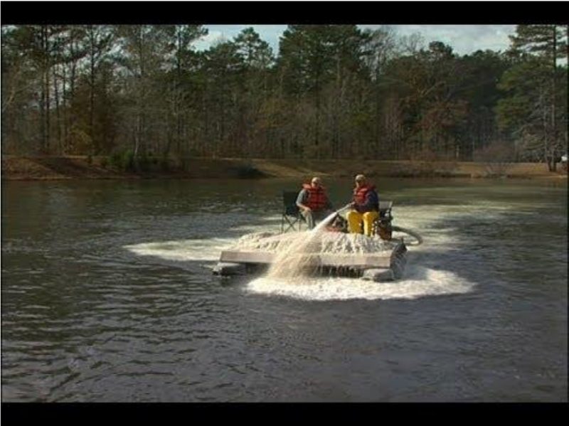 A photo of two men in a small boat applying lime to a pond.