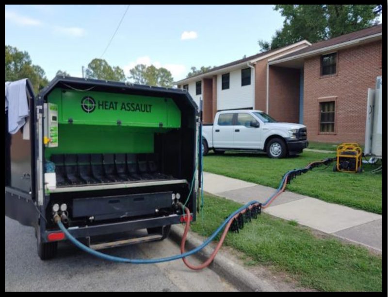 A truck with a green and black box that has two pumps, blue and red, pumping heated glycol inside an apartment.