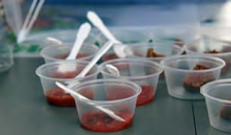 Several clear plastic cups containing samples and white spoons on a table.