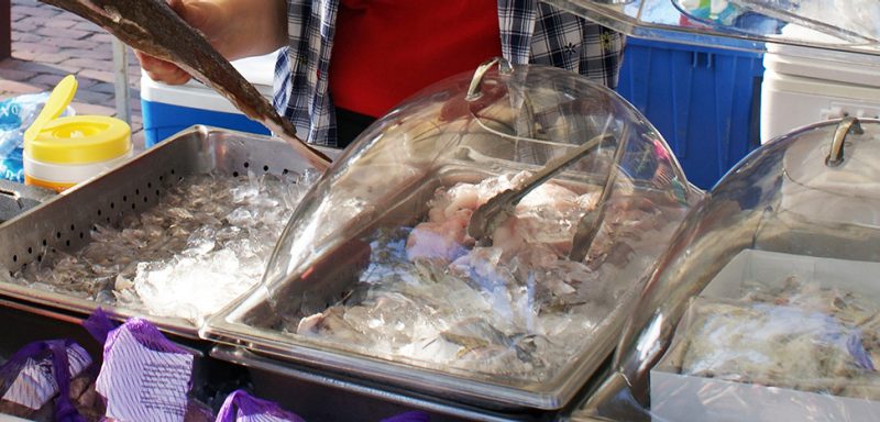 Three metal trays holding ice, two of which have seafood products on the ice and are covered with plastic lids.