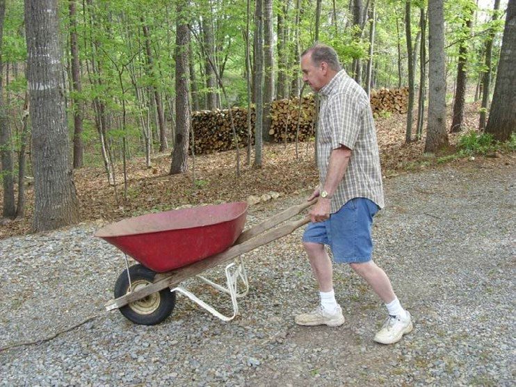 A man pushing a wheel barrel outside and in the woods.