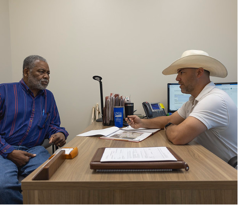Two gentlemen is discussion sitting at a desk.