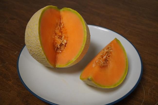 A mature melon with orange flesh cut open on a plate.