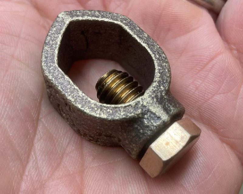 A bronze ground rod clamp in the palm of a hand.