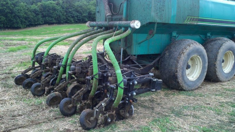  A photo of a large, green truck in a field with six bright green hoses extending from the back, each attached to a wheel assembly.