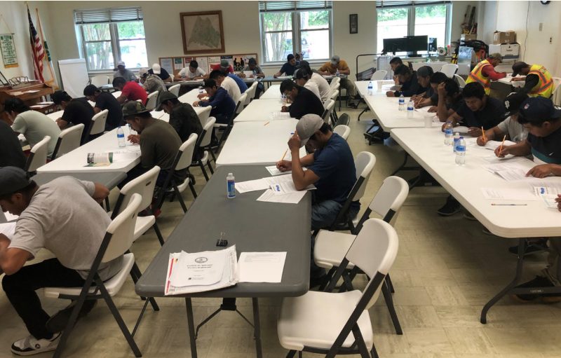 A large group of individuals sitting at tables and writing on paper.